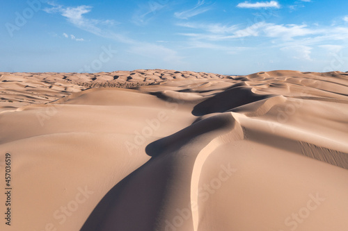 Large sand dunes with texture, patterns, light and shadow. Blue sky with white clouds