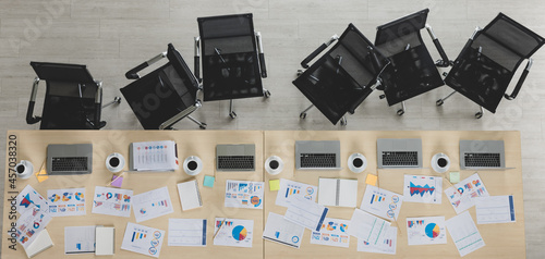 Table top view of wooden conference table with charts and graphs papers and laptop on it and six chairs lying in straight line beside the table in office. Concept for business meeting