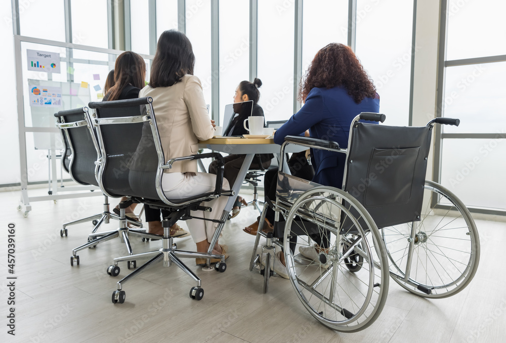 Asian business women and handicap woman sitting on wheelchair are in meeting together on the table in office. Concept for business meeting