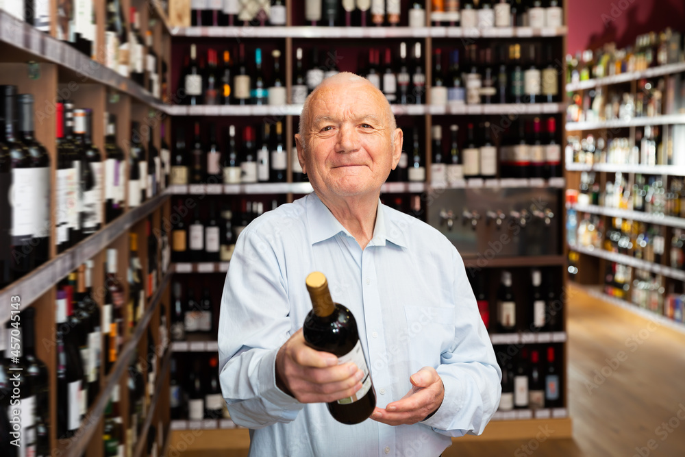 Portrait of elderly male customer selecting wine in supermarket