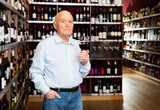 Elderly man checks the color and taste of red wine in a liquor store.
