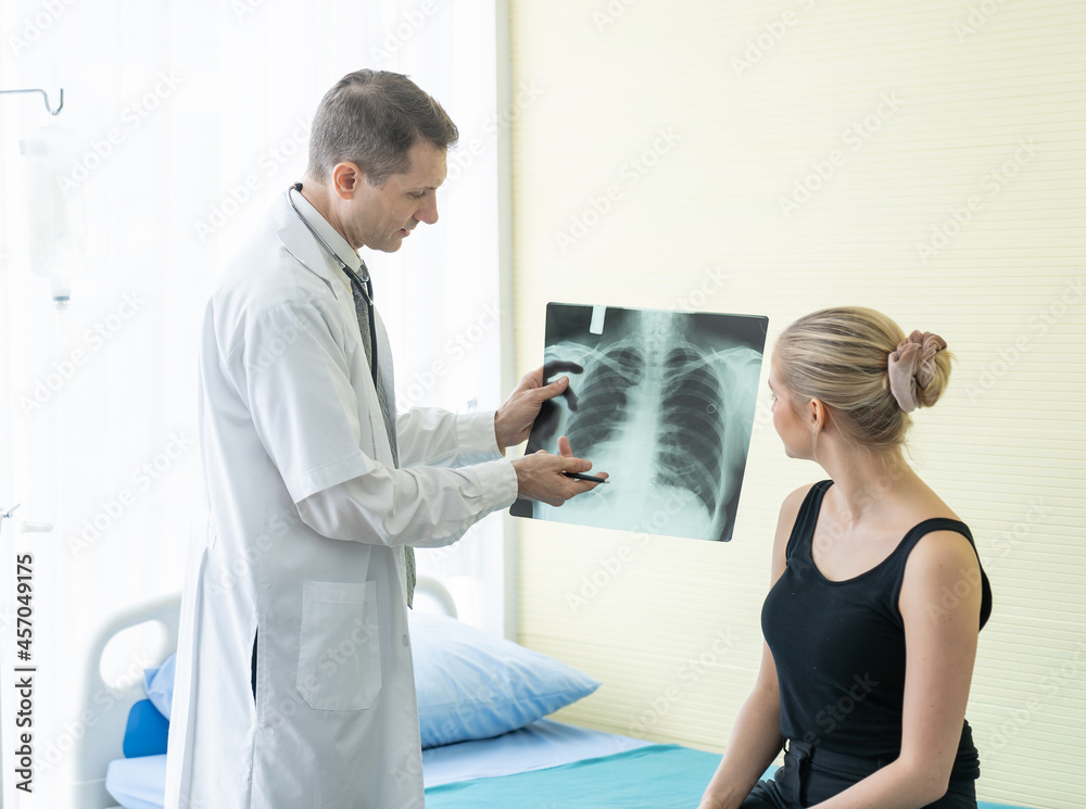 Obraz premium Senior doctor or physician discussing to young patient woman and examining a chest x-ray photo scan at the clinic or hospital. Medicine and Healthcare concept. Doctor and patient