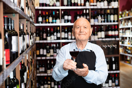 Successful cheerful positive elderly male owner of winery inviting to tasting wine of own production