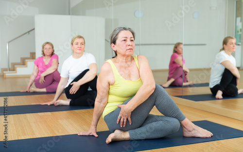 Women exercising during yoga class in modern fitness center - marichiasana pose