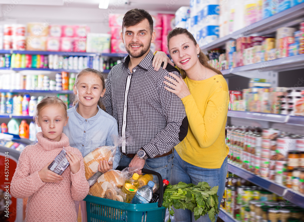 Young friendly family of four with full shopping basket in supermarket