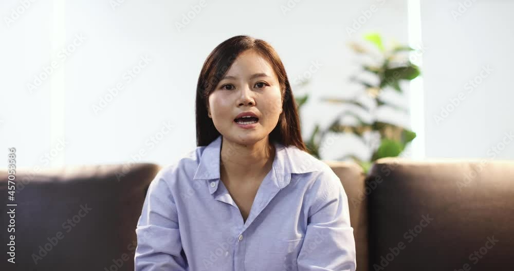 Cute and young Asian, Chinese ethnic look, business woman sitting at sofa and speak to web camera in video call session with hands gestures. Female businesswoman doing online chat. Cute and young Asian, Chinese ethnic look, business woman sitting at sofa and speak to web camera in video call session with hands gestures. Female businesswoman doing online chat.