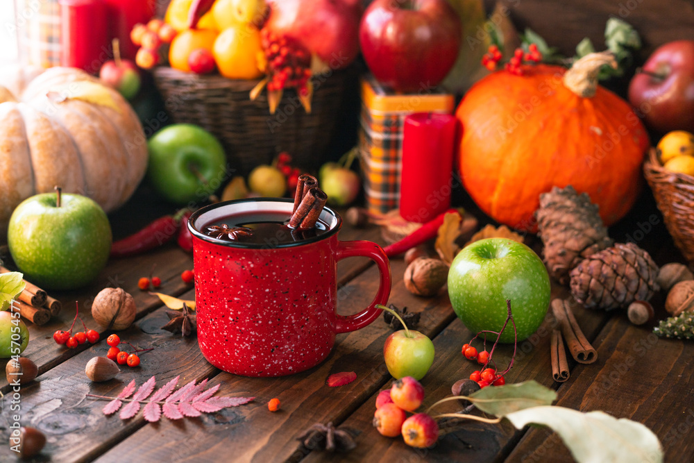 red mug with mulled wine. Cinnamon sticks stick out of the cup and a star of star anise floats. Fruits and spices are all around on a wooden table red mug with mulled wine. Cinnamon sticks stick out of the cup and a star of star anise floats. Fruits and spices are all around on a wooden table