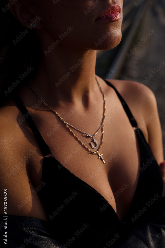 sexy female tanned breasts in black bra in the rays of the sunset close-up, vertical photo