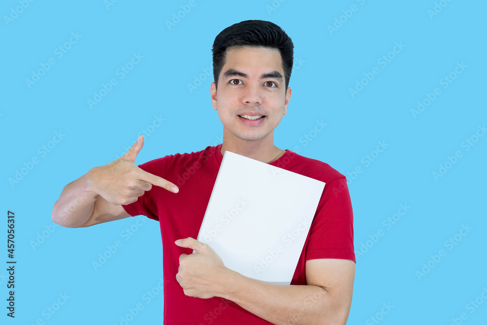 Portrait handsome young asian man wearing a red shirt holding a blank paper or billboard feeling happy and pointing to paper isolated on blue background. Businessman concept. Portrait handsome young asian man wearing a red shirt holding a blank paper or billboard feeling happy and pointing to paper isolated on blue background. Businessman concept.