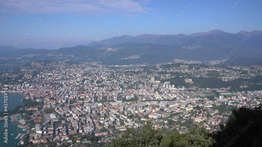 Aerial panorama view over City of Lugano on a sunny late summer morning with Lake Lugano and Mountains. Movie shot September 11th, 2021, Lugano, Switzerland. Aerial panorama view over City of Lugano on a sunny late summer morning with Lake Lugano and Mountains. Movie shot September 11th, 2021, Lugano, Switzerland.