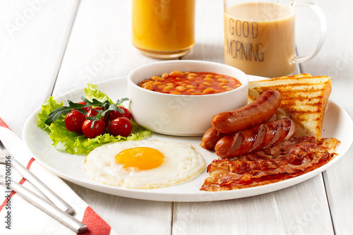 Traditional Full English breakfast, on a white background, fried eggs with fried bacon, sausages, white beans ,cherry tomatoes, horizontal, no people,
