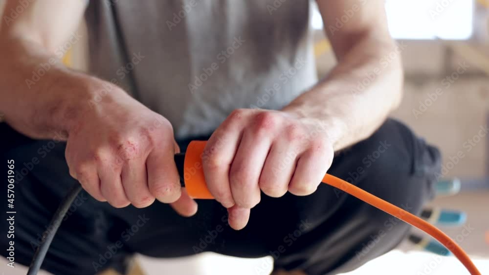 A handyman construction worker in a helmet plugs the drilling tool into an outlet. A handyman construction worker in a helmet plugs the drilling tool into an outlet.