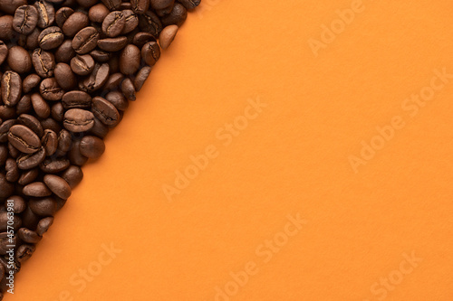 Roasted coffee beans on orange background with copy space. Close up top view.