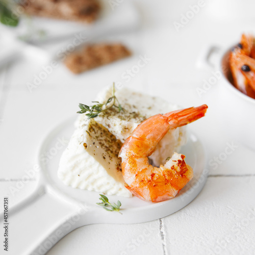Shrimp on a white table serving for lunch, next to cheese and spices.