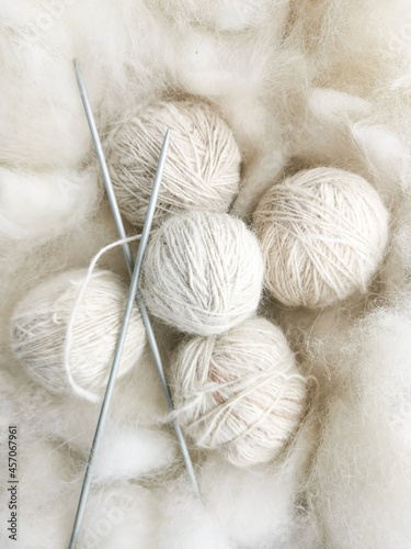 Balls of white natural wool and knitting needles