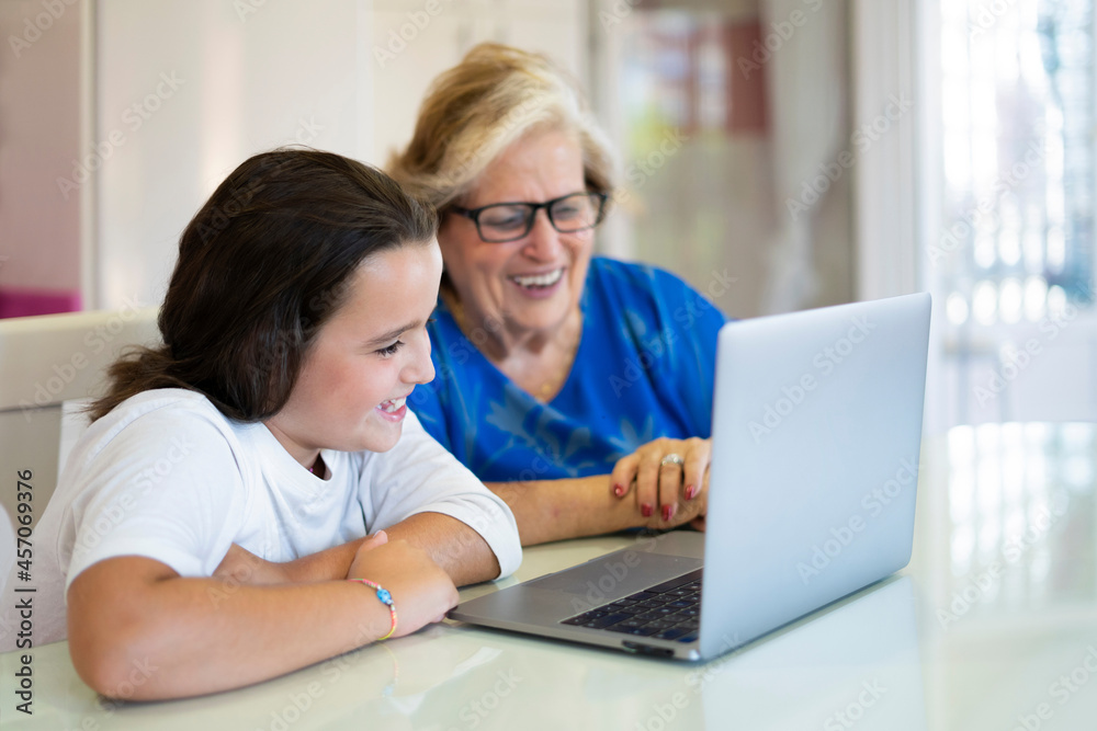 Positive girl teaching grandmother working on laptop at home Positive girl teaching grandmother working on laptop at home