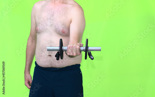 Front view of a middle-aged dad bod man in his 30s lifting a dumbbell weight to get fit. Concept fitness, weigh reduction, self-improvement. Green background.