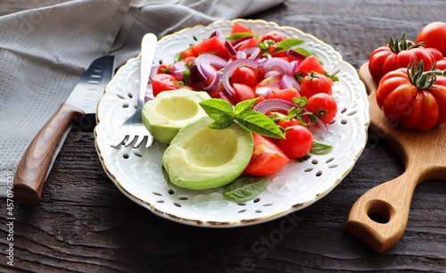 Fresh healthy avacado and tomato salad with onions on dark rusric background photo