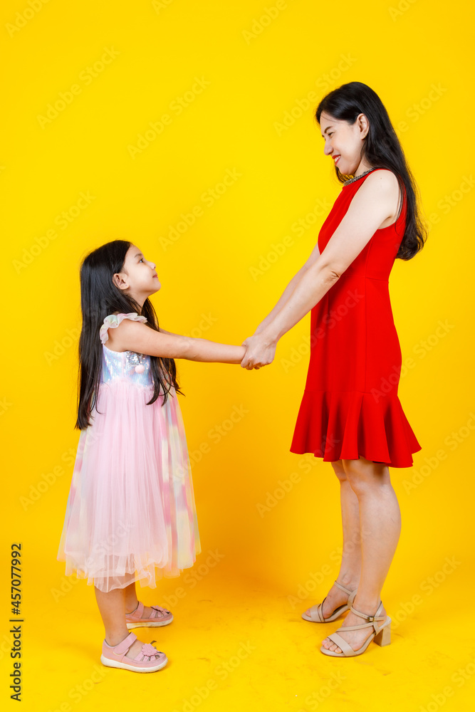 Asian mom and daughter taking portrait photo together on yellow background Asian mom and daughter taking portrait photo together on yellow background