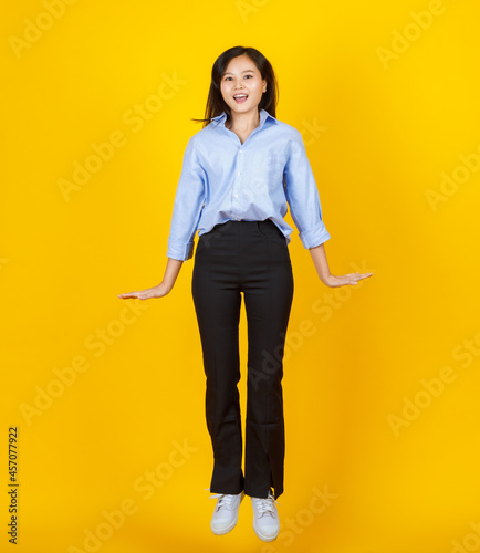 Lovely young Asian girl jumping and freezed in the air with excited and cheerful face on yellow background