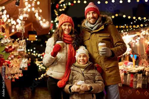 family, winter holidays and celebration concept - happy mother, father and little daughter with takeaway drinks at christmas market on town hall square in tallinn, estonia