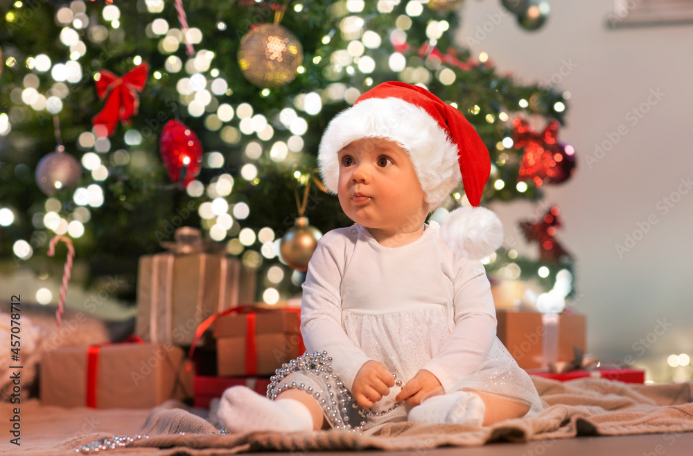 holidays and childhood concept - sweet baby girl with gifts at home over christmas tree lights holidays and childhood concept - sweet baby girl with gifts at home over christmas tree lights