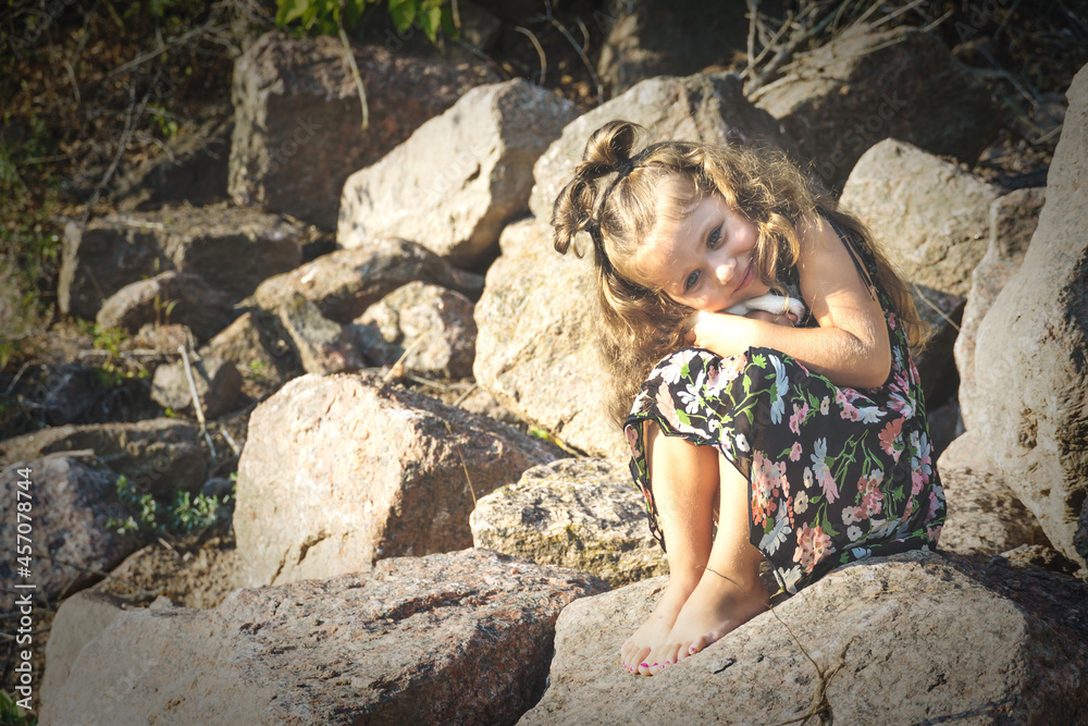 a little girl on the rocks with a toy in her hands, the sun illuminates her
