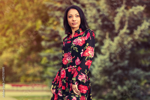 Happy young fashion woman in floral dress in city park