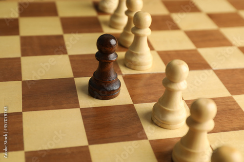 Black pawn among white ones on chess board, closeup. Concept of racism