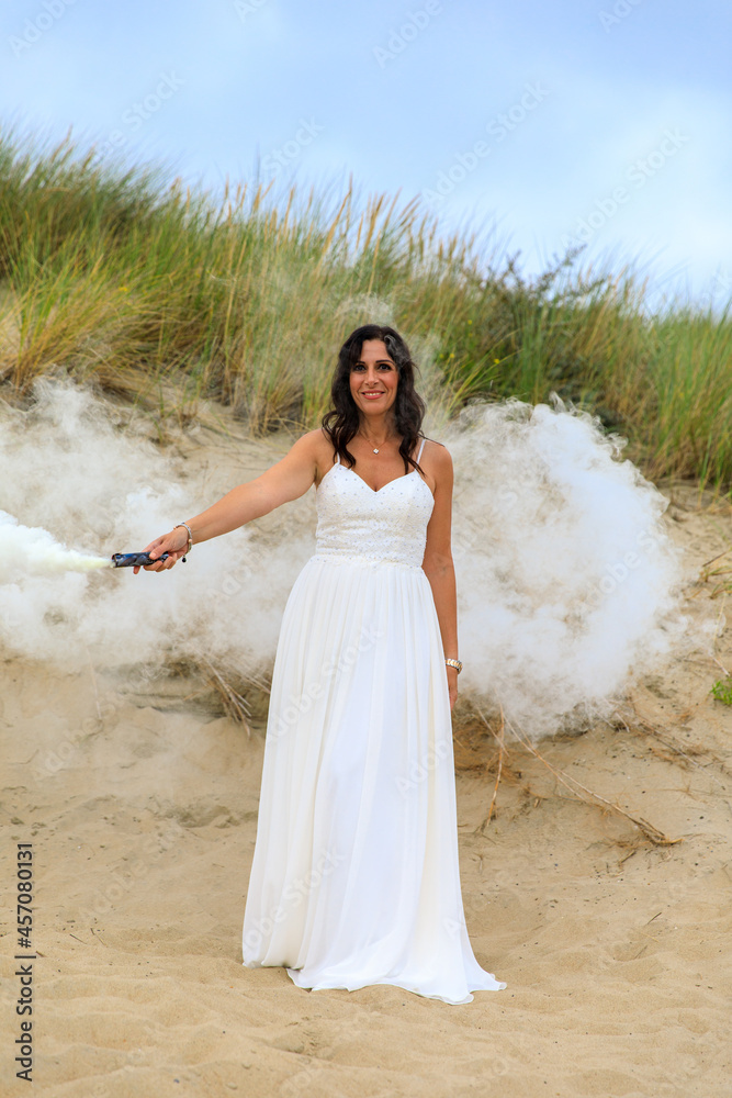 Junge schöne Frau im Hochzeitskleid am Strand mit einer Rauchfackel und weißen Rauch