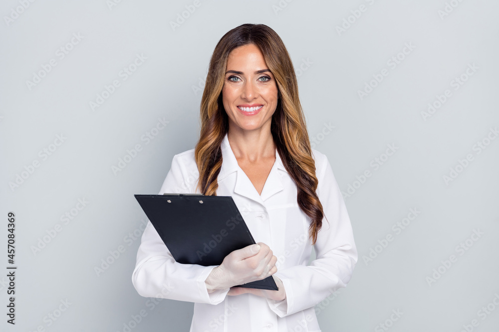 Photo of pretty cheerful woman doc dressed white coat holding clipboard smiling isolated grey color background Photo of pretty cheerful woman doc dressed white coat holding clipboard smiling isolated grey color background