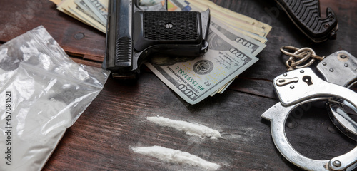 фотографія Drugs smuggling and trafficking, Handcuffs, pistol money and cocaine on wooden t