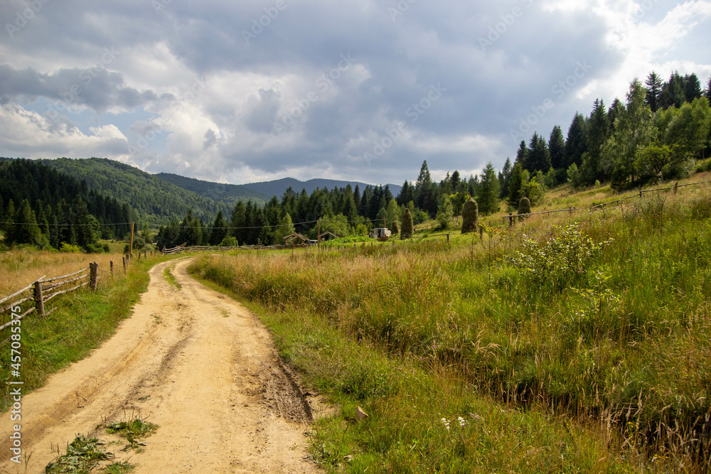 Road in a mountain village, forest, mountains and wooden fence