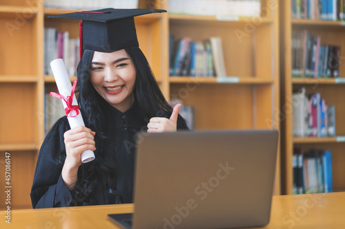 University graduate in graduation gown and mortarboard celebrates in a virtual graduation ceremony. Happy female student on her graduation day at home. Concept of online education