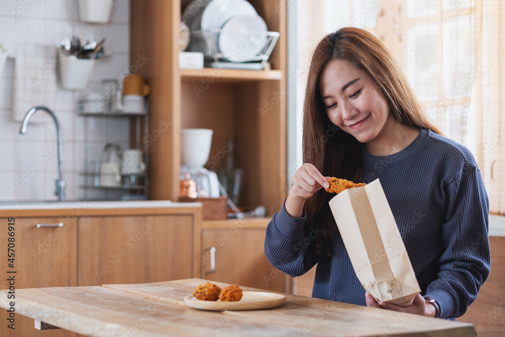 A young woman picking fried chicken from paper food bag and putting in a plate at home for food delivery concept A young woman picking fried chicken from paper food bag and putting in a plate at home for food delivery concept