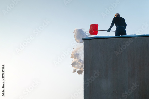 Man throwing snow of the rooftop on a sunny winter day. Worker cleaning top of a building.