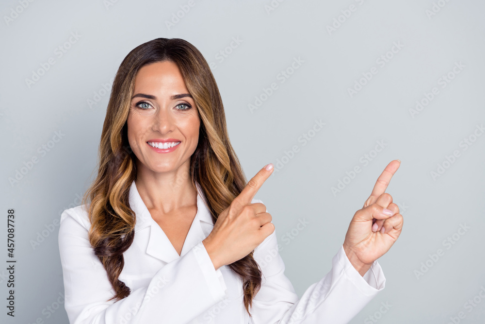 Photo of mature nice brown hairdo lady point empty space wear white nurse coat isolated on grey background Photo of mature nice brown hairdo lady point empty space wear white nurse coat isolated on grey background