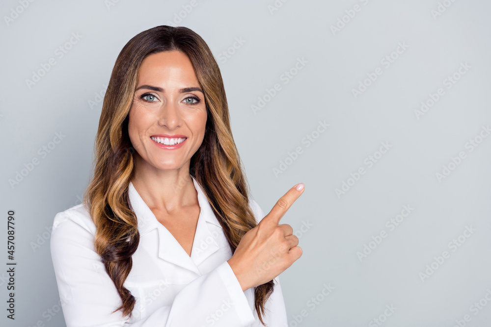 Photo of mature nice brown hairdo lady point empty space wear white nurse coat isolated on grey background Photo of mature nice brown hairdo lady point empty space wear white nurse coat isolated on grey background