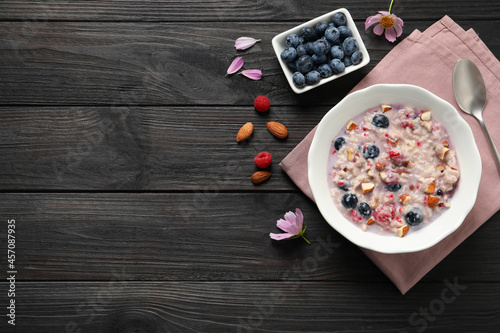 Tasty oatmeal porridge with toppings on black wooden table  flat lay. Space for text
