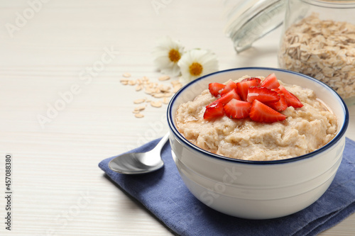 Tasty oatmeal porridge with strawberries served on white wooden table. Space for text