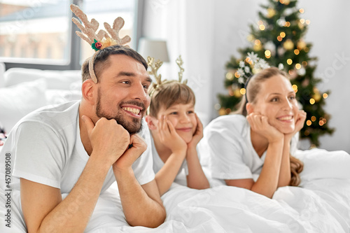 family, winter holidays and people concept - happy mother, father and little son in bed in christmas morning