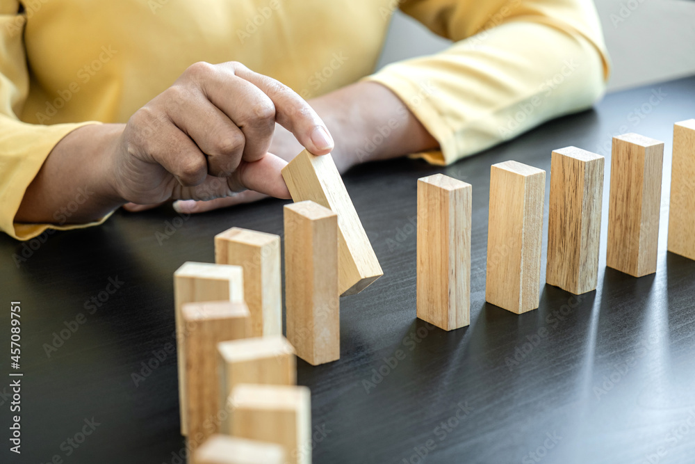 Risk and Strategy in Business, Image of hand stopping falling collapse wooden block dominoes effect from continuous toppled block, prevention and development to stability Risk and Strategy in Business, Image of hand stopping falling collapse wooden block dominoes effect from continuous toppled block, prevention and development to stability