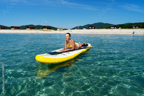 Relaxed travel woman in swimsuit sunbathing on surfboard enjoying sup surfing extreme sport