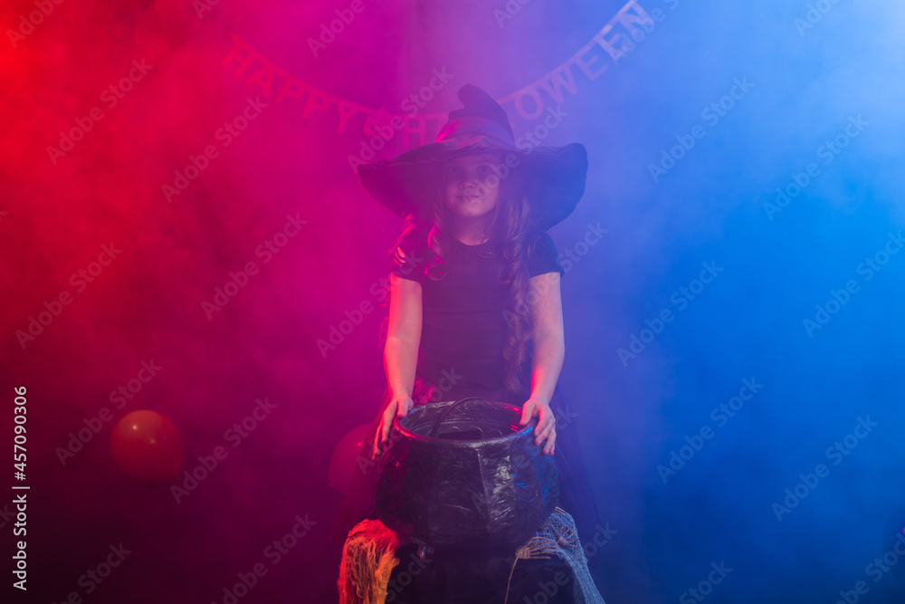 Child girl witch preparing a potion in the cauldron at halloween holidays.