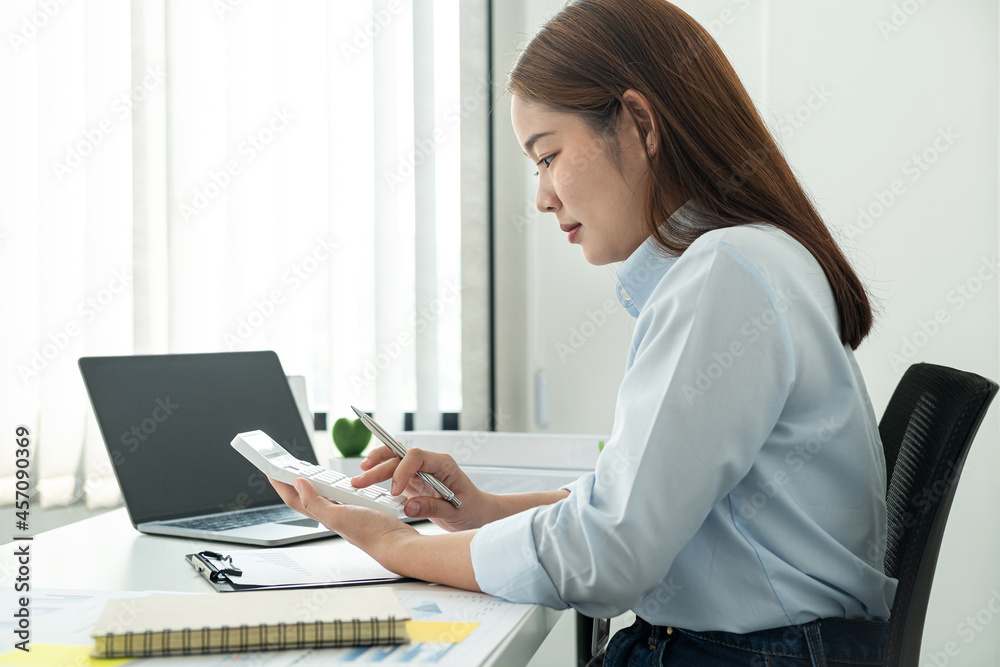 Woman office worker sitting to working and pressing a calculator to calculate the profit of a new business project Woman office worker sitting to working and pressing a calculator to calculate the profit of a new business project