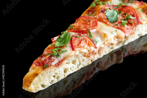 Slice of pizza with tomatoes and parsley, on a black mirrored background. Beautiful light, product reflection.