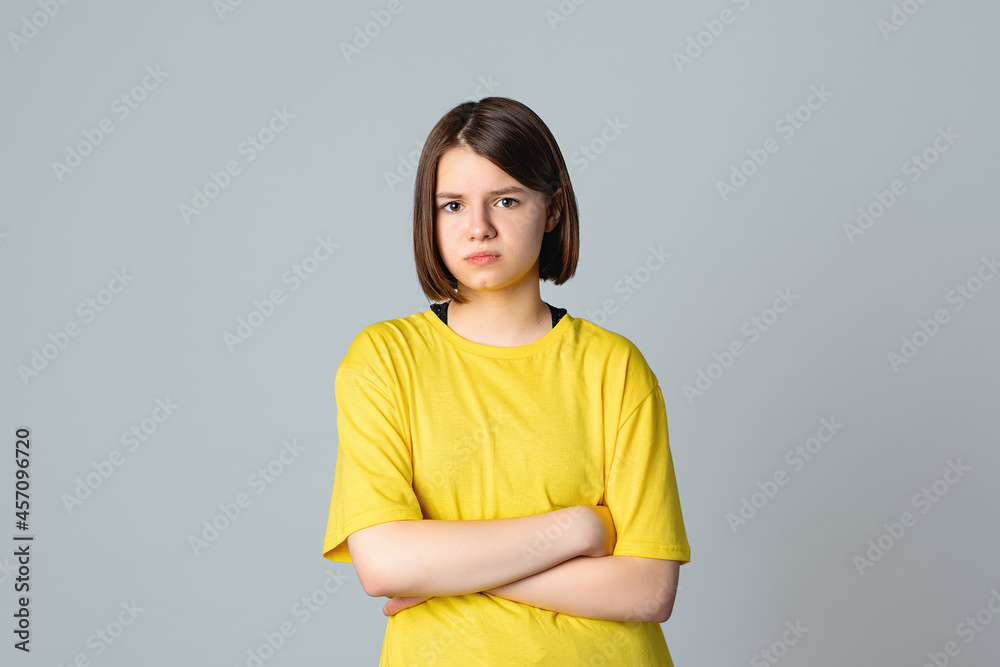Portrait of a offended teen girl with crossed arms, standing over light grey background. Teen disappointment. Loneliness boredom Portrait of a offended teen girl with crossed arms, standing over light grey background. Teen disappointment. Loneliness boredom