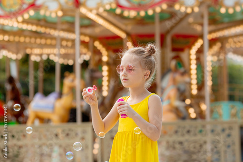 a little girl in sunglasses blows soap bubbles in the park in the summer