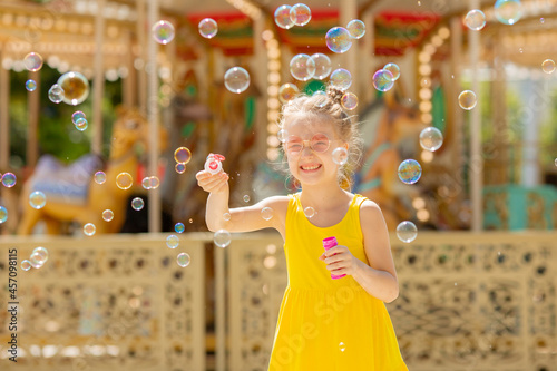 a little girl in sunglasses blows soap bubbles in the park in the summer © Olesya Pogosskaya