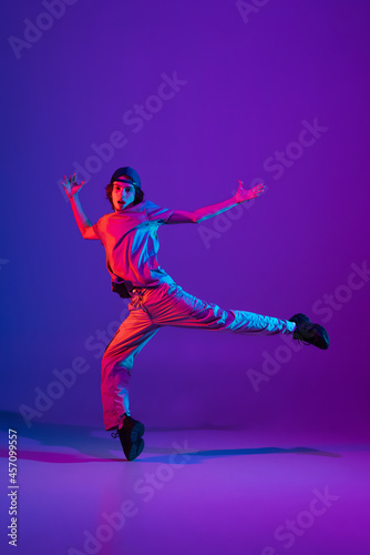 Young stylish man, break dancing, hip-hop dancer practicing solo in casual clothes isolated over purple background in neon pink light at dance hall © master1305